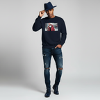 Man wearing navy blue Naughty Is a Lifestyle sweatshirt paired with ripped jeans and a hat against a plain background