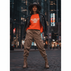 Woman wearing orange GOD Heard What I Didn't sweatshirt styled with black leather jacket and cargo pants in urban night setting